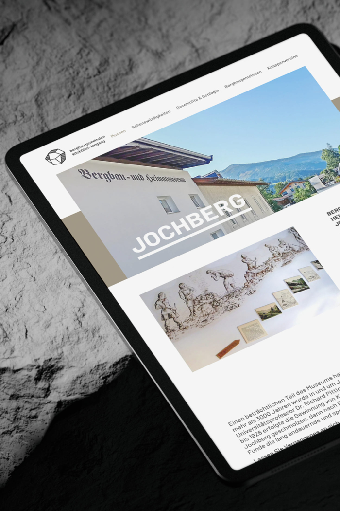 Auf einem Tablet wird die Unterseite zur Bergbaugemeinde Jochberg präsentiert. Das Design ist in erdigen Tönen gehalten und zeigt ein großes Header-Bild.