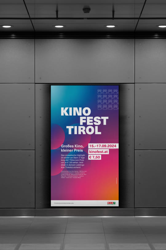 Auf einer Monitorwerbung in einer öffentlichen Begegnungszone wird das Sujet des Kinofest Tirol angezeigt. Das farbenfrohe Design reicht von Blau über Lila/Rosa bis Gelb und präsentiert in weißer Schrift die wichtigsten Fakten zum Kinofest Tirol.
