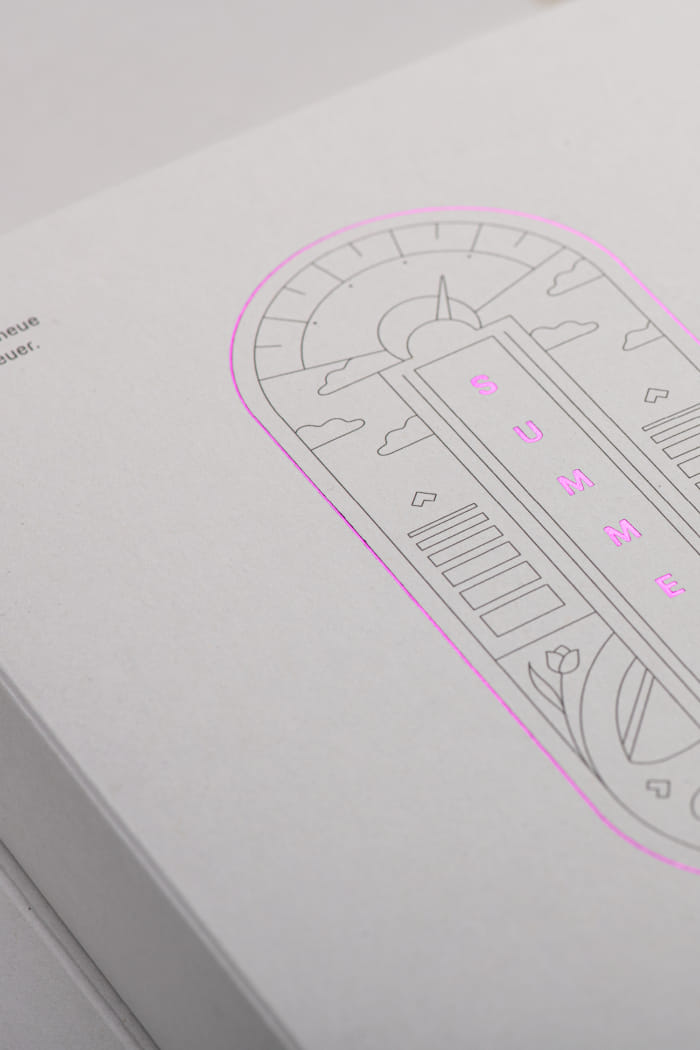 Direct Mailing in einem hellen Design mit lila-spiegelnder Schrift auf der Vorderseite. Die Box enthält neben der Schrift auch Illustrationen als grafische Elemente.