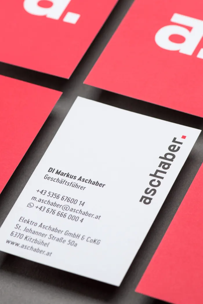 Mehrere Aschaber Visitenkarten im neuen Branding angeordnet auf grauem Hintergrund. Vorderseite ganz in rot nur mit dem a und viereckigem Punkt in weiß mittig. Rückseite mit Schrifzug am rechten oberen Rand und den Infos zu Geschäftsführer Markus Aschaber.