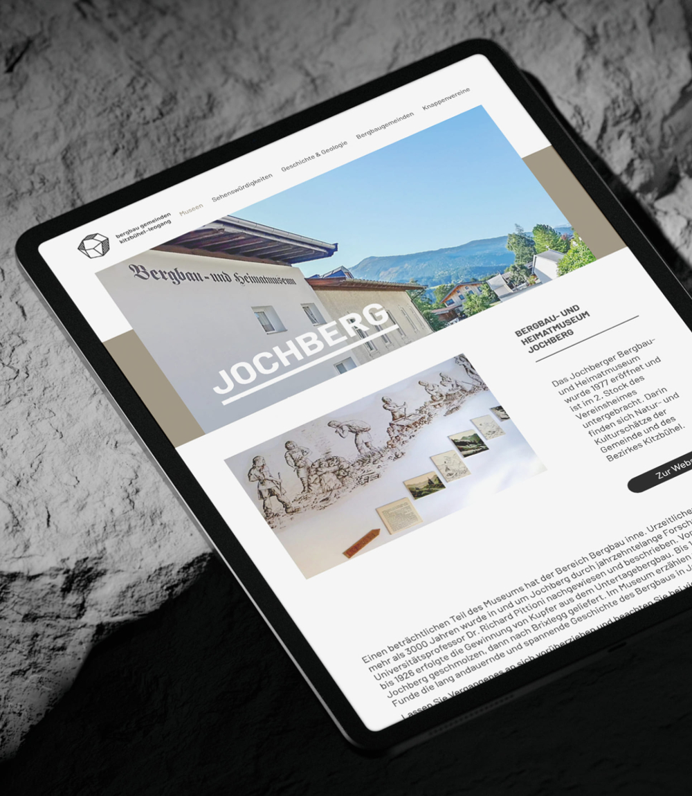 Auf felsigem Hintergrund sieht man ein Tablet mit einem Abschnitt zu Jochberg auf der Website Bergbau Gemeinden Kitzbühel-Leogang.