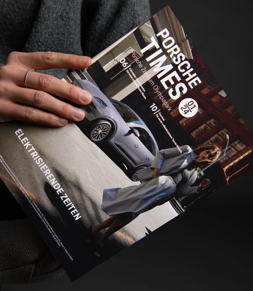 Person hält die Porsche Times Ausgabe mit dem Titelmotiv des vollelektrischen Macan und der Headline Elektrisierende Zeiten in der Hand.