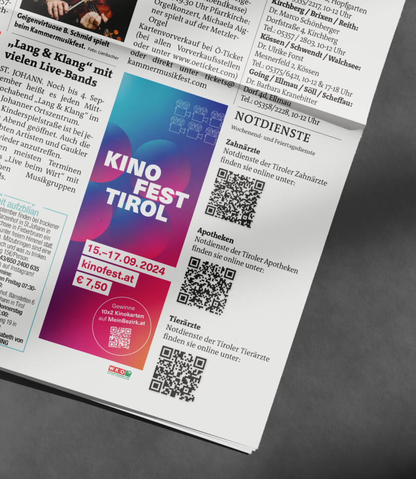 Auf grauem Hintergrund liegt eine aufgeschlagene Zeitung und im unteren rechten Viertel ist eine hochformatige Werbeanzeige des Kino Fest Tirol mit Event-Daten zu sehen.