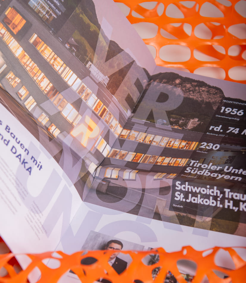 Dynamische Nahaufnahme des DAKA Magazins mit überlagerten Seiten, die Fakten zur Unternehmensgeschichte und Standorte zeigen. Das charakteristische orangefarbene Gitternetz bildet einen markanten Rahmen um die in Schrägperspektive fotografierten Magazinseiten.