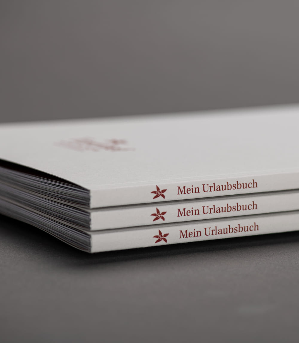 Drei gestapelte weiße Broschüren mit dem Titel 'Mein Urlaubsbuch'.
