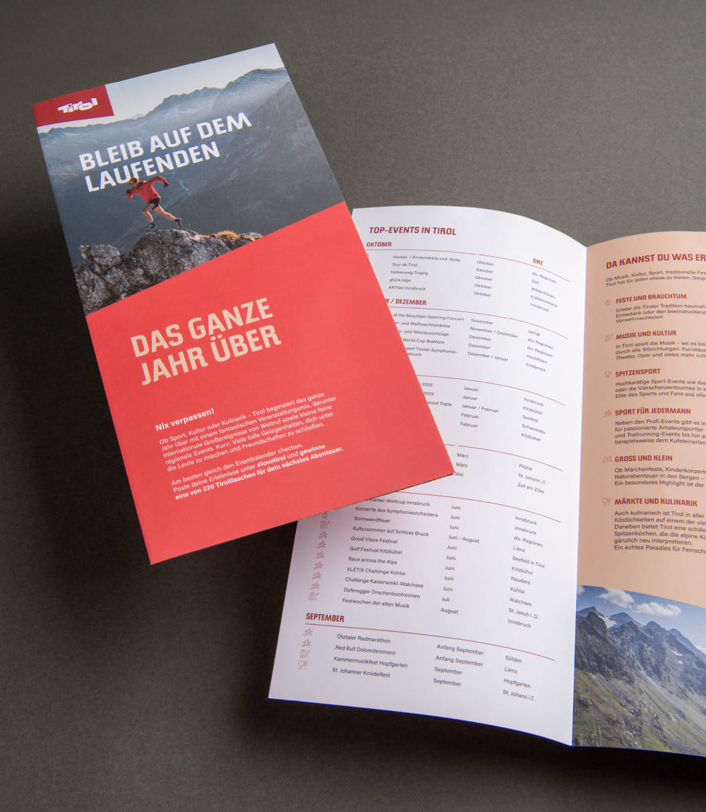 Geschlossener und geöffneter Tirol Folder mit Titel Bleib auf dem Laufenden, auf dunkelgrauer Tischplatte.