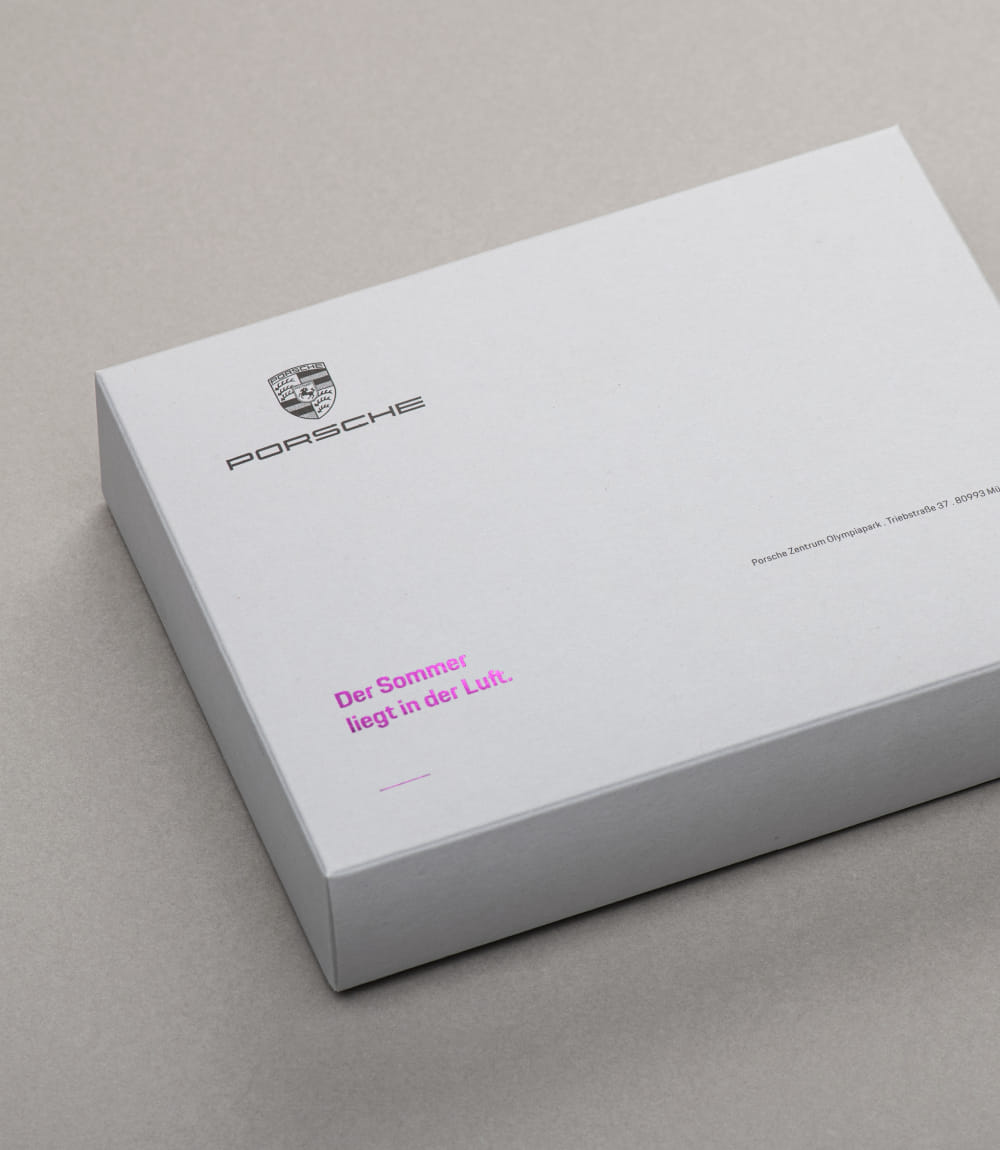 Mailingbox mit Porsche Logo und dem Schriftzug Der Sommer liegt in der Luft in pinker Prägung. Rechts unten die Adresse des Porsche Zentrums Olympiapark München.