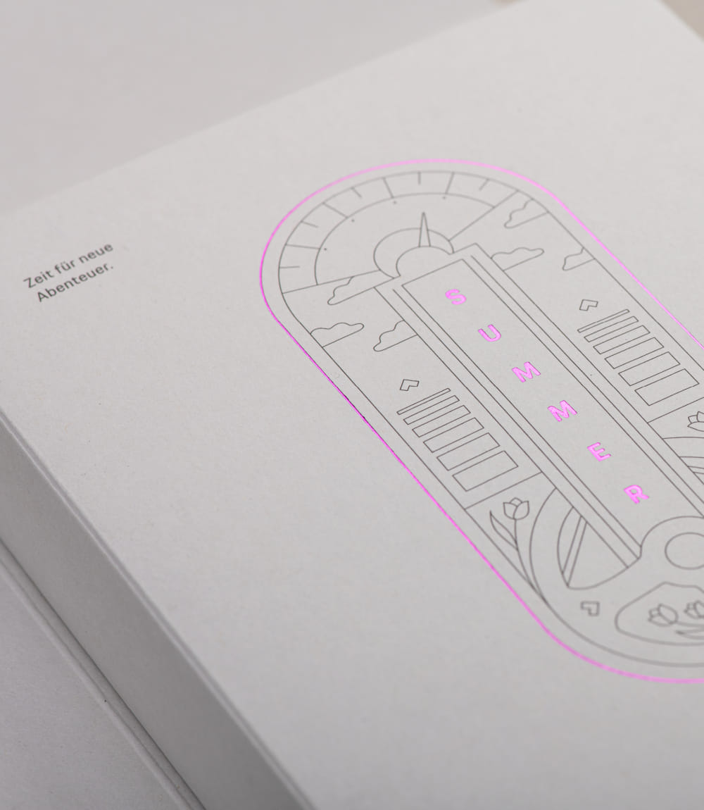 Detailansicht der Mailing-Verpackung für das Porsche Zentrum Olympiapark München mit grafischer Illustration und pinker Heißfolienprägung SUMMER. Links der Text Zeit für neue Abenteuer.
