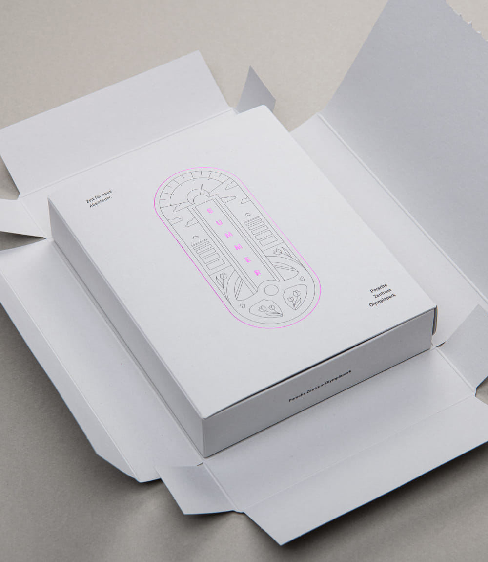 Geöffneter Versandkarton mit Mailingbox des Porsche Zentrums Olympiapark; darauf Illustration mit pinker Prägung SUMMER und der Text Zeit für neue Abenteuer.