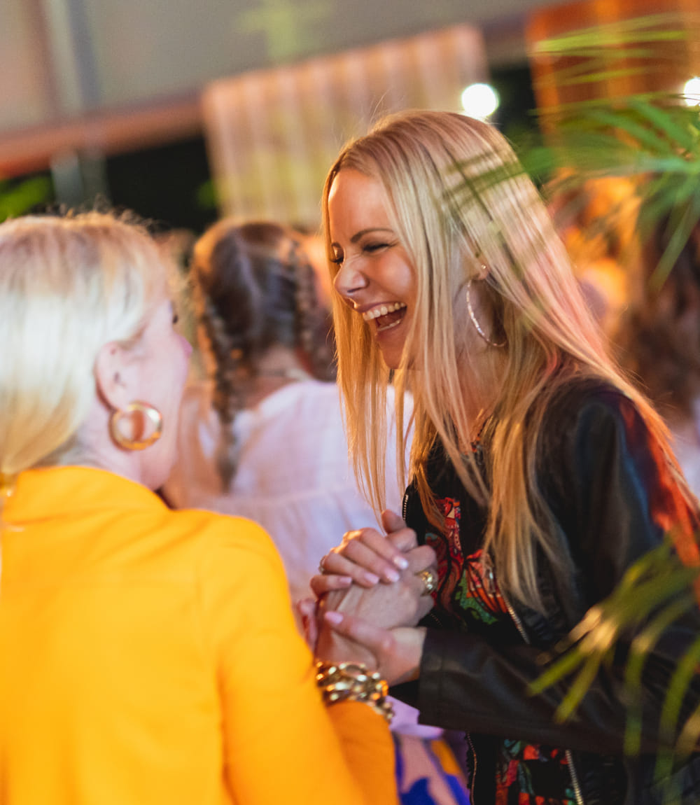 Zwei Frauen im Hippie-Look lachen herzlich und halten sich an den Händen 