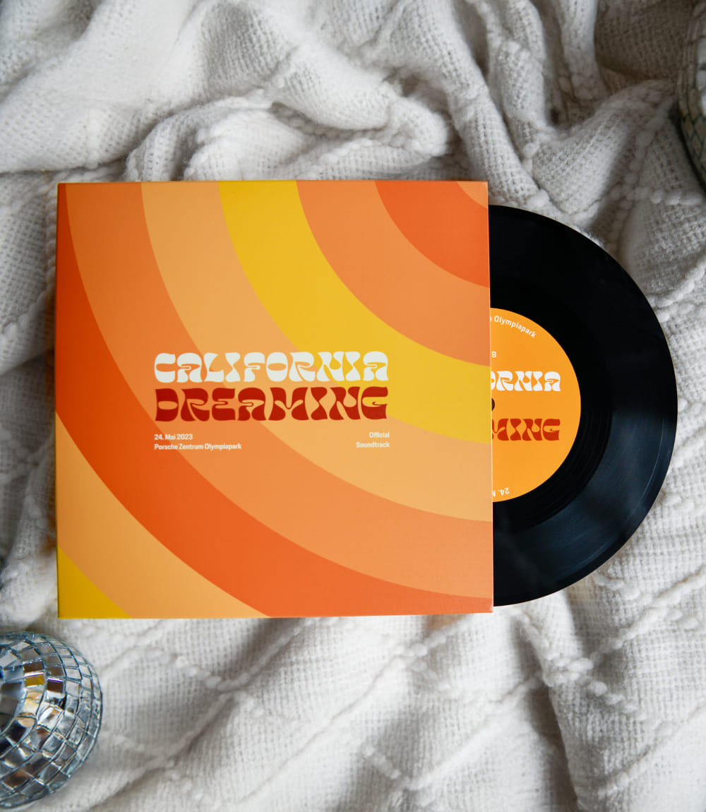 Schallplattenhülle mit Vinyl für CALIFORNIA DREAMING mit 70er-Jahre-Retro-Design in Orange- und Gelbtönen. Die LP für das Porsche Zentrum Olympiapark vom 24. Mai 2023 ist als Official Soundtrack gekennzeichnet. 