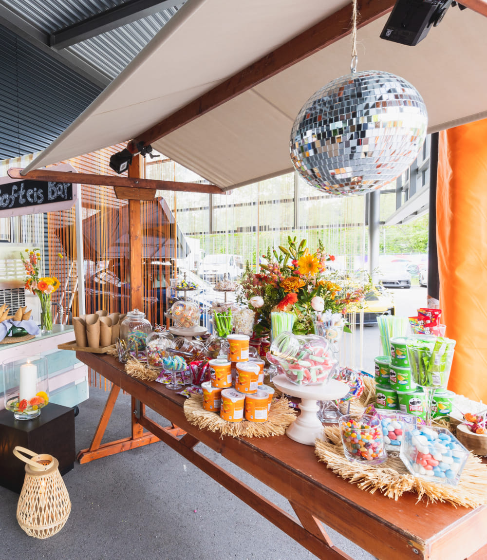 Buffettisch mit bunten Süßigkeiten, Snacks und Blumendekorationen im California-Dreaming-Stil.