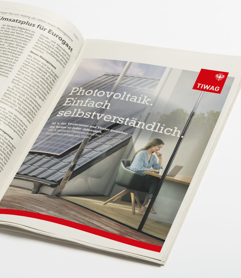 TIWAG-Werbeanzeige in einer Zeitschrift mit dem Slogan Photovoltaik. Einfach selbstverständlich und einer Frau am Laptop neben Photovoltaikanlagen auf dem Dach.