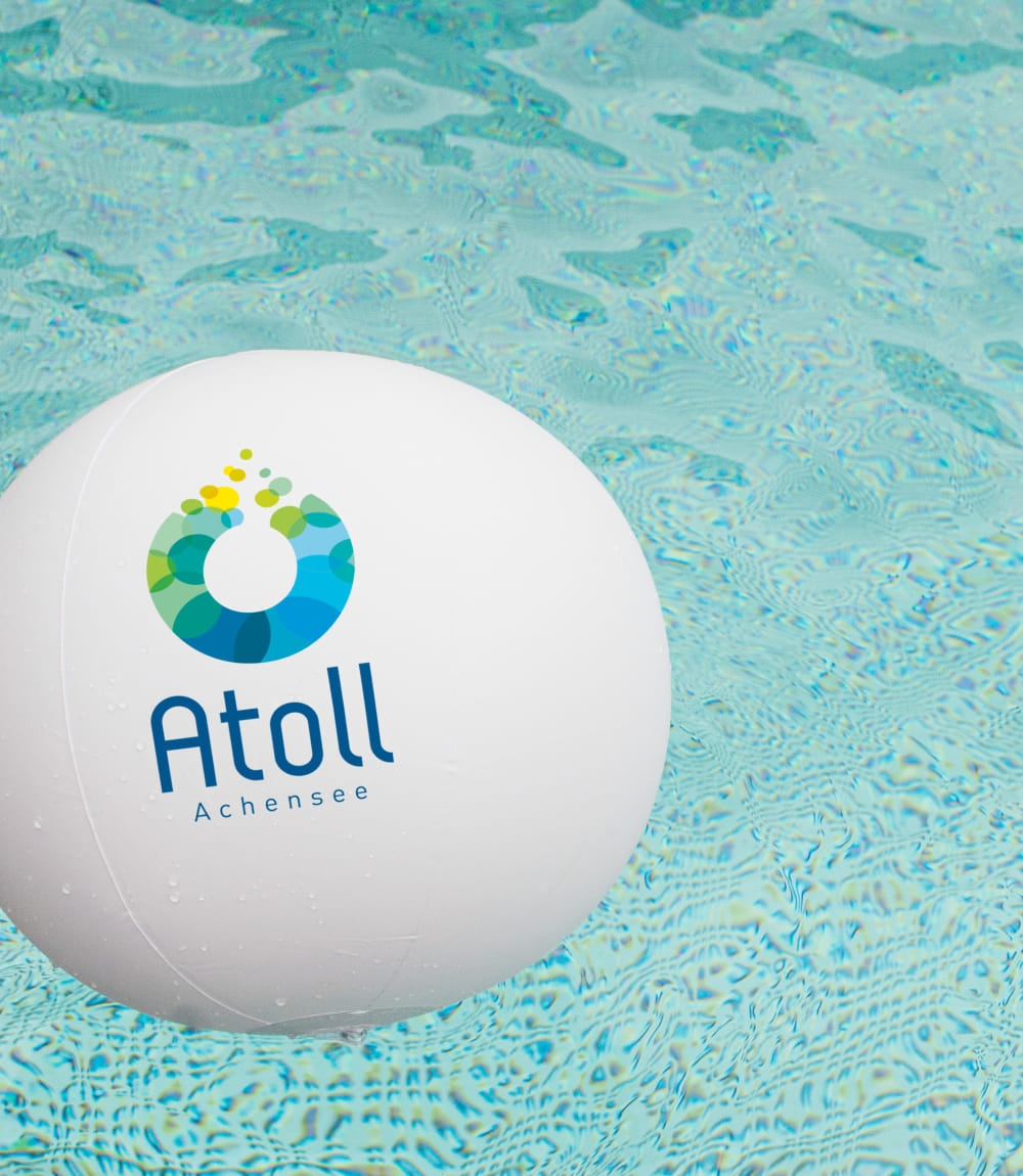 Weißer Wasserball mit Atoll Achensee Logo schwimmt im türkisblauen Poolwasser. 