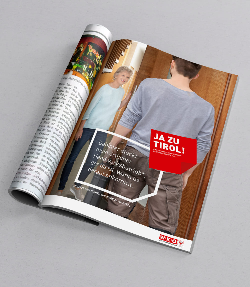 Aufgeschlagenes Magazin mit Werbeanzeige der JA ZU TIROL! Kampagne. Auf dem Bild steht eine ältere Dame in hellblauem Oberteil lächelnd in einer Tür und begrüßt einen Handwerker von hinten gesehen. Im Vordergrund rotes Kampagnenlogo mit dem Text: Dahinter steckt mein örtlicher Handwerksbetrieb*, der da ist, wenn es darauf ankommt.