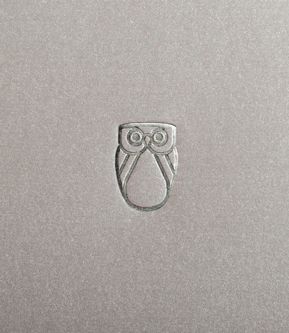 Geprägtes Orovivo-Eulensignet auf strukturierter, schimmernder Oberfläche in Beige.
