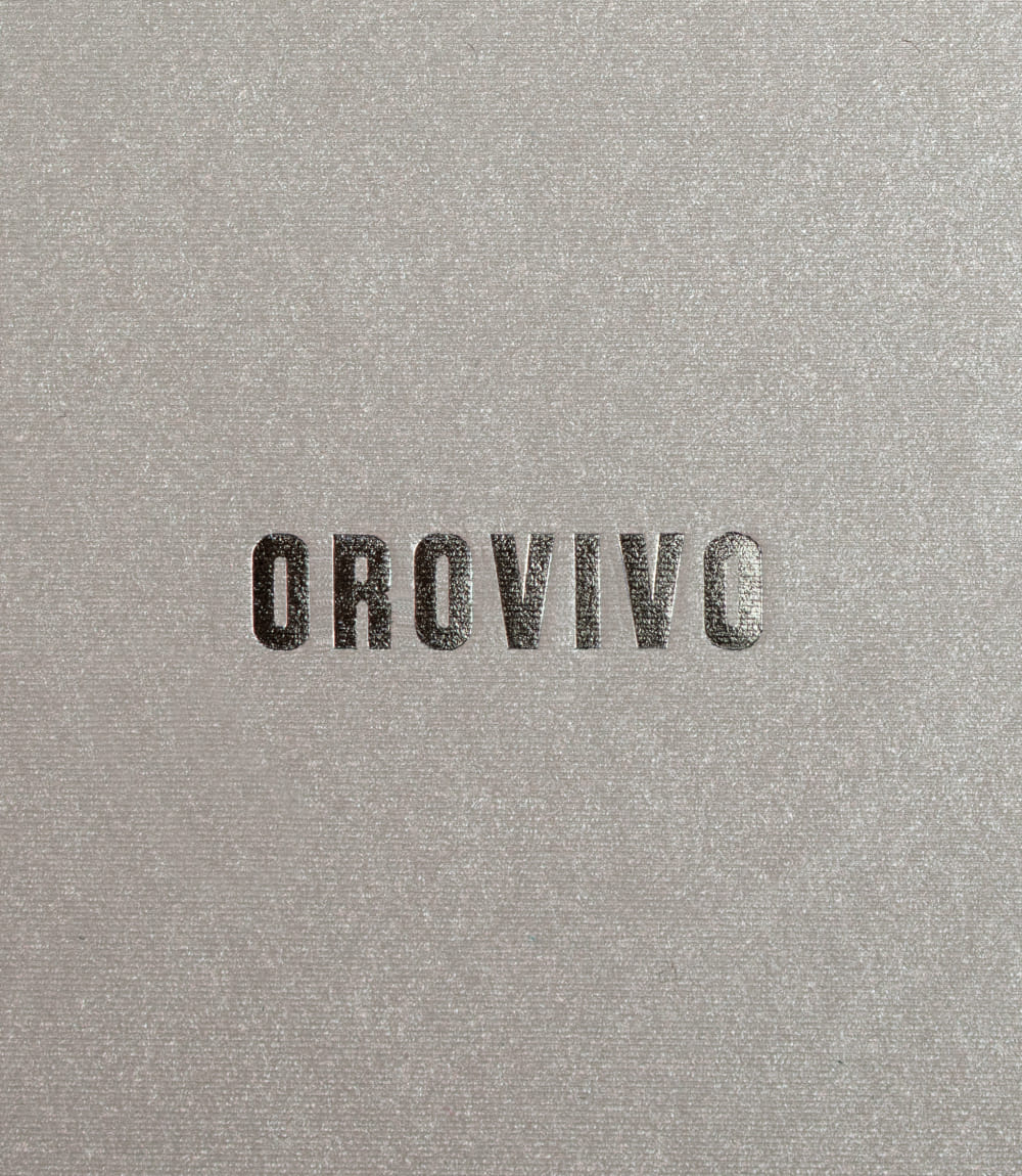 Schwarze Prägung des OROVIVO-Logos auf schimmernder, strukturiert-beiger Oberfläche.
