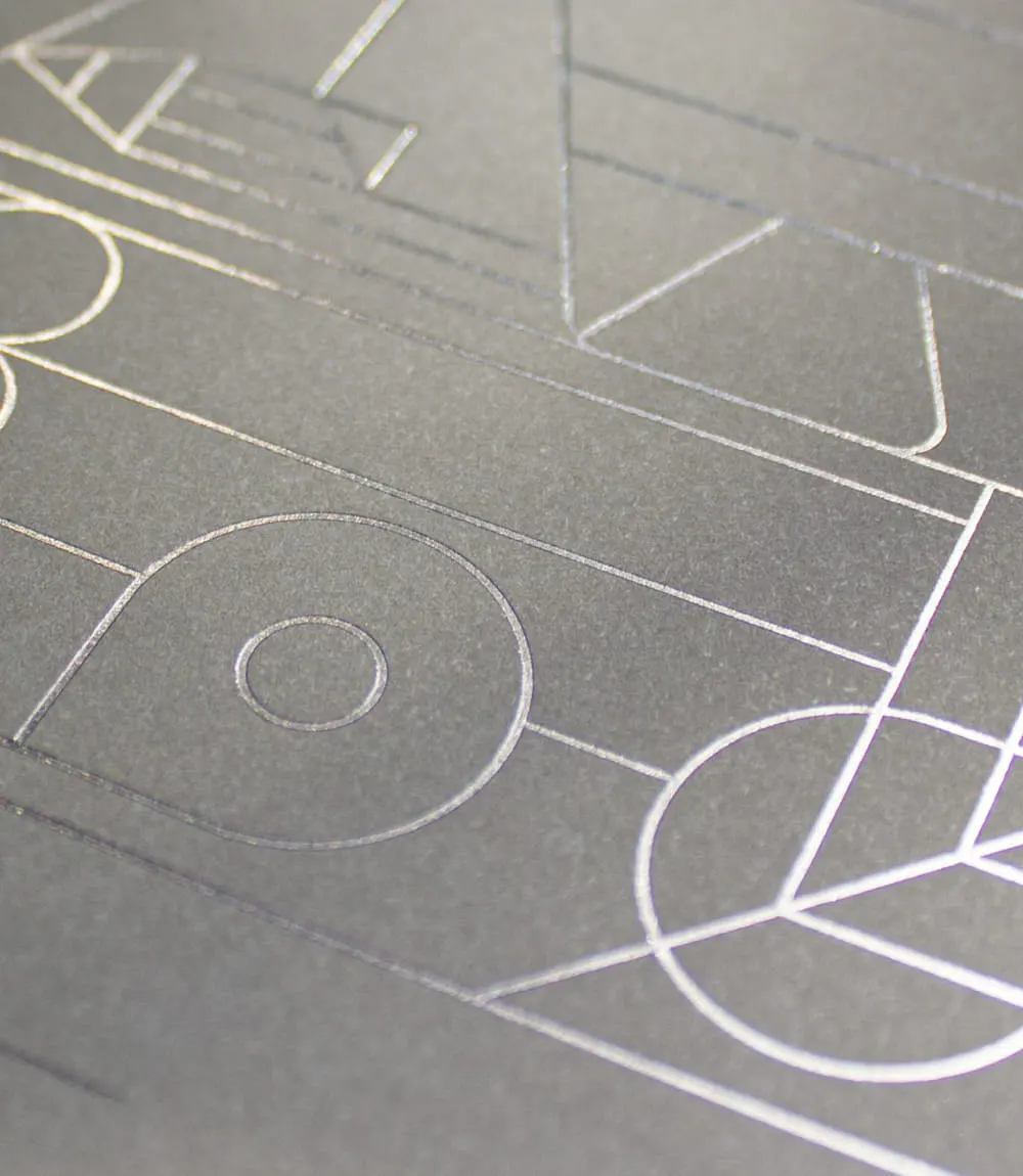 Detailaufnahme eines geprägten Covers mit filigranen Linien und geometrischen Formen in schimmernder Metallicfolie auf grauem Feinstpapier.