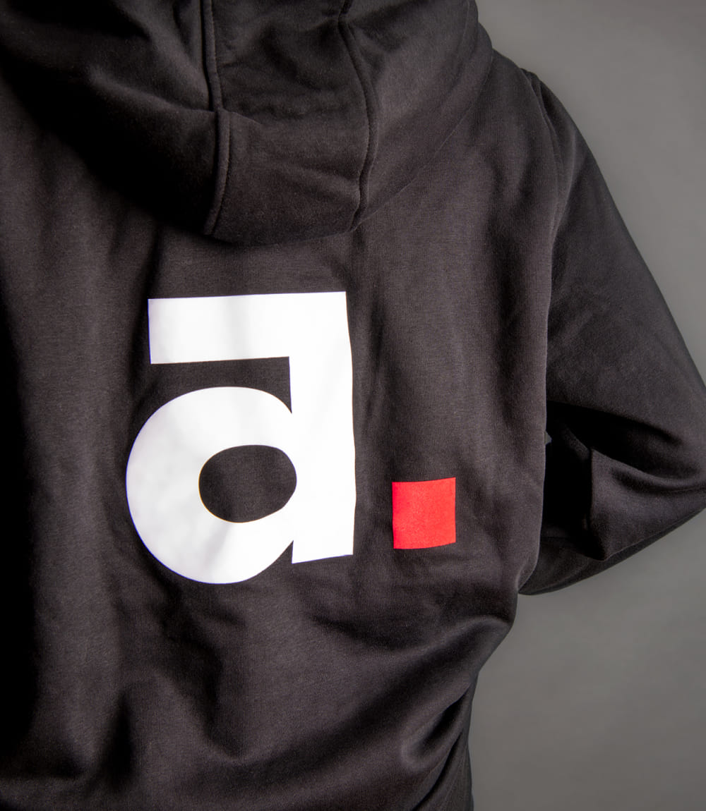 Rückseite eines schwarzen Hoodies mit Aschaber Logo - aufgedrucktes weißes a und viereckiger roter Punkt.