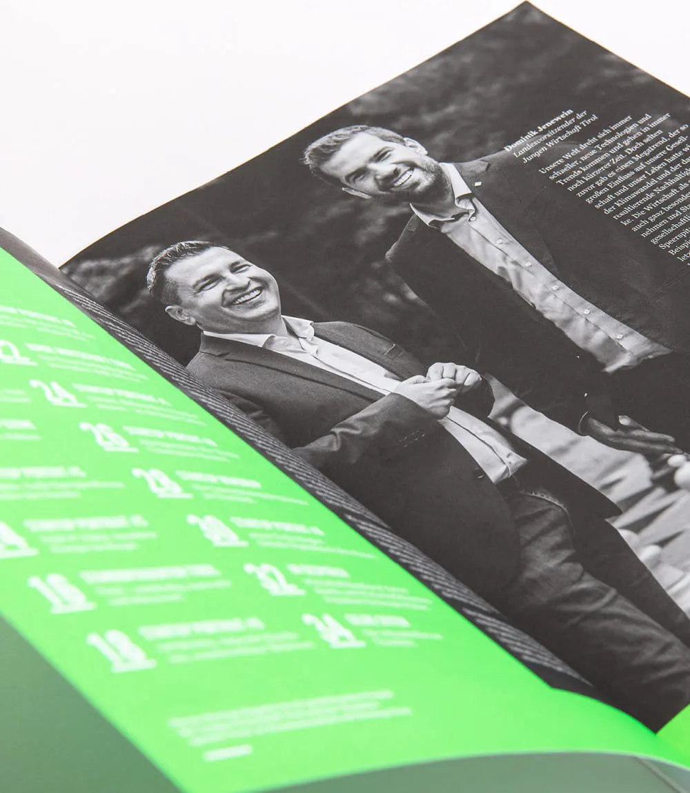 Ein aufgeschlagenes Magazin auf der linken Seite neongrün mit weißer Schrift. Die rechte Seite zeigt ein Schwar-Weiß Fotografie von zwei lächelnden Männern und zugehörigen Text in weiß.