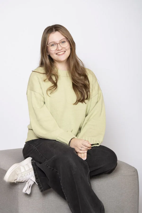 Frau mit Brille und grüner Bluse sitzt auf einem Sofa.
