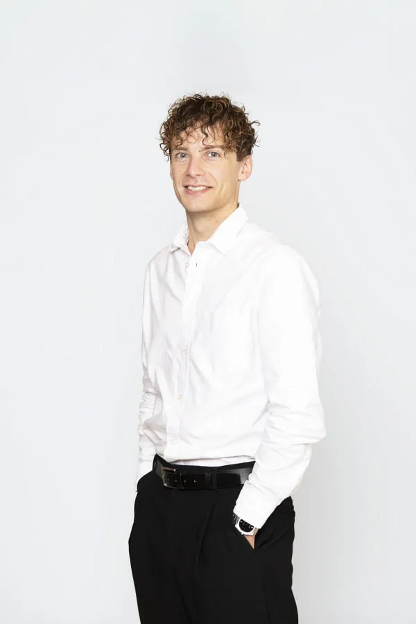 Mann mit lockigem Haar in weißem Hemd, lächelt freundlich.